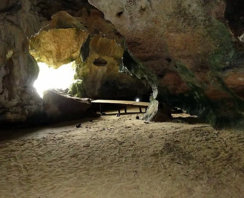 Interior of a cave with a sandy floor, a wooden walkway, and natural light coming in through the opening