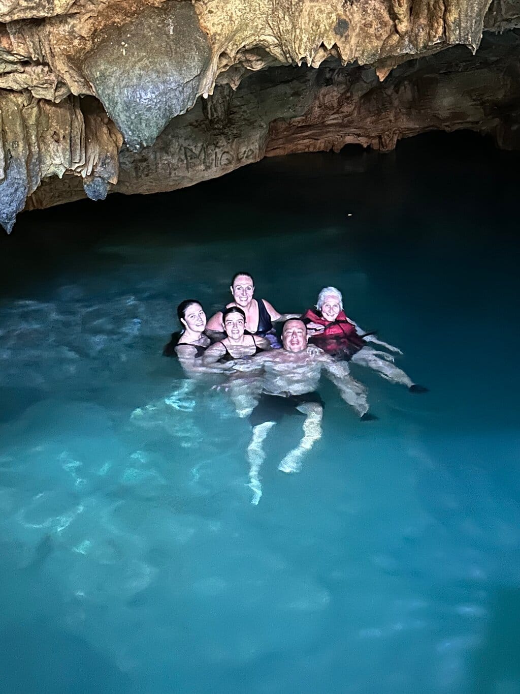 Group of tourists swimming in the crystal-clear turquoise water of a cave with stalactites on the ceiling