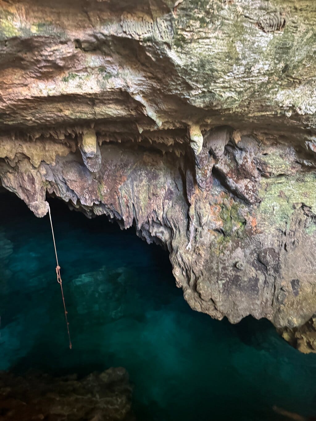 Cave with stalactites and a rope hanging over a pool of crystal-clear turquoise water