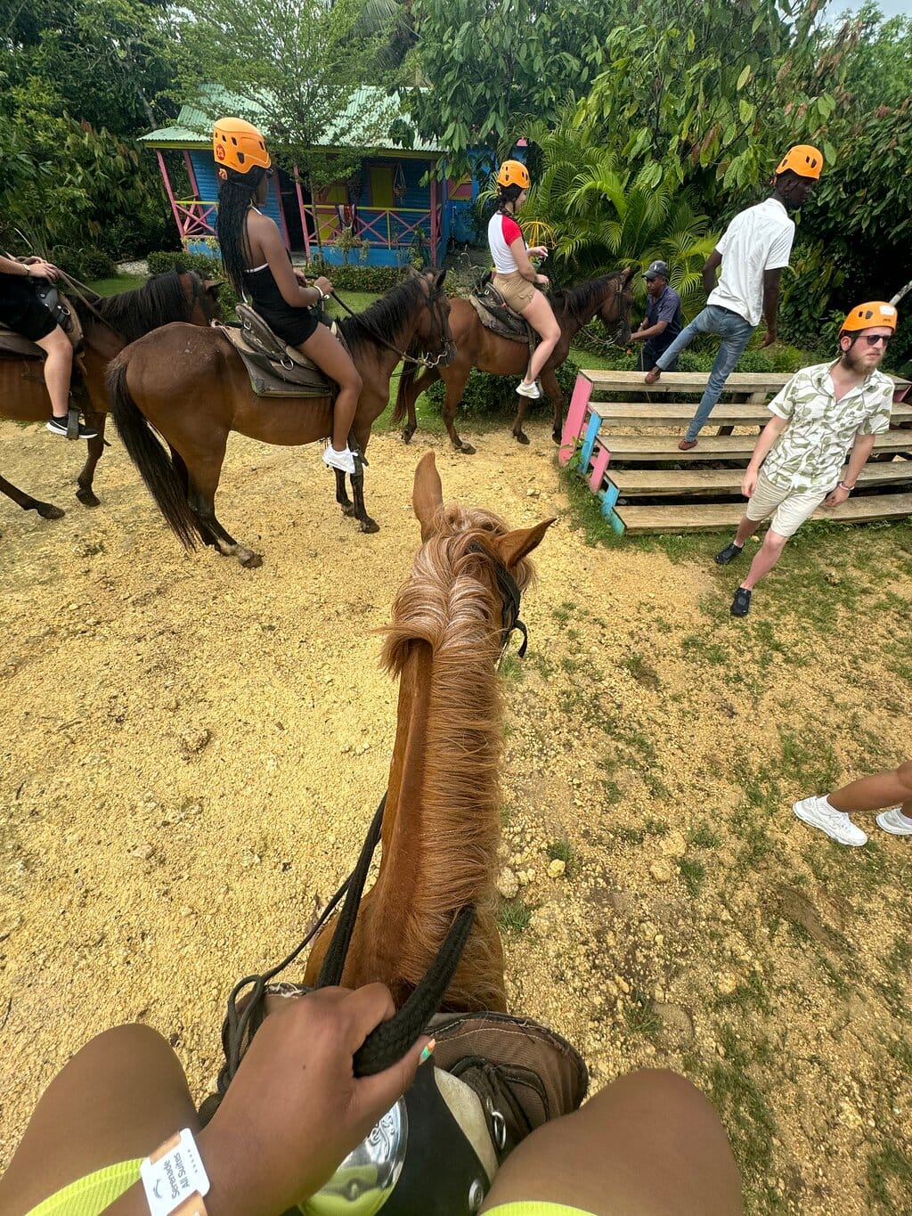 First-person view from a horse during the horseback ride, with riders in orange helmets and a small colorful house