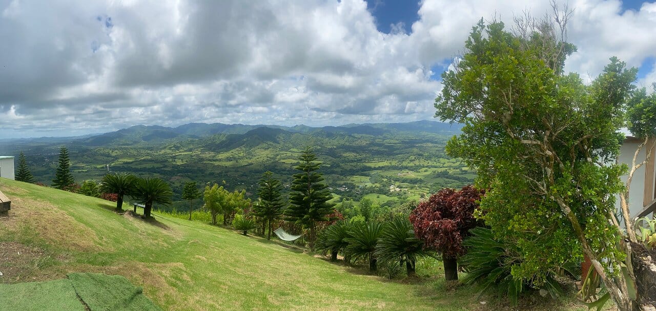 Panoramic view from the top of Montaña Redonda over green valleys and mountains, with a hammock on the hillside