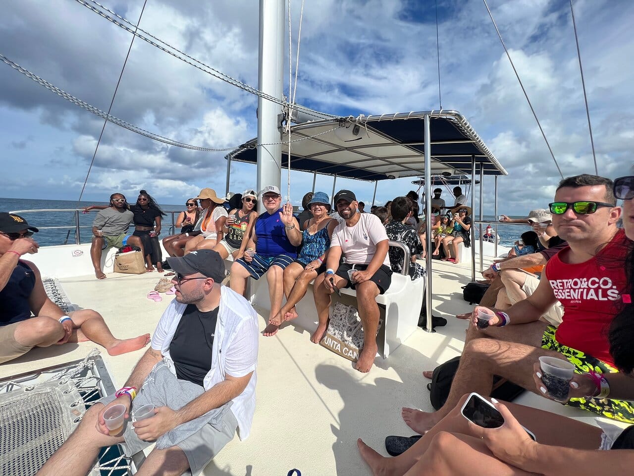 Group of tourists sitting on the deck of a catamaran with drinks in hand during the crossing