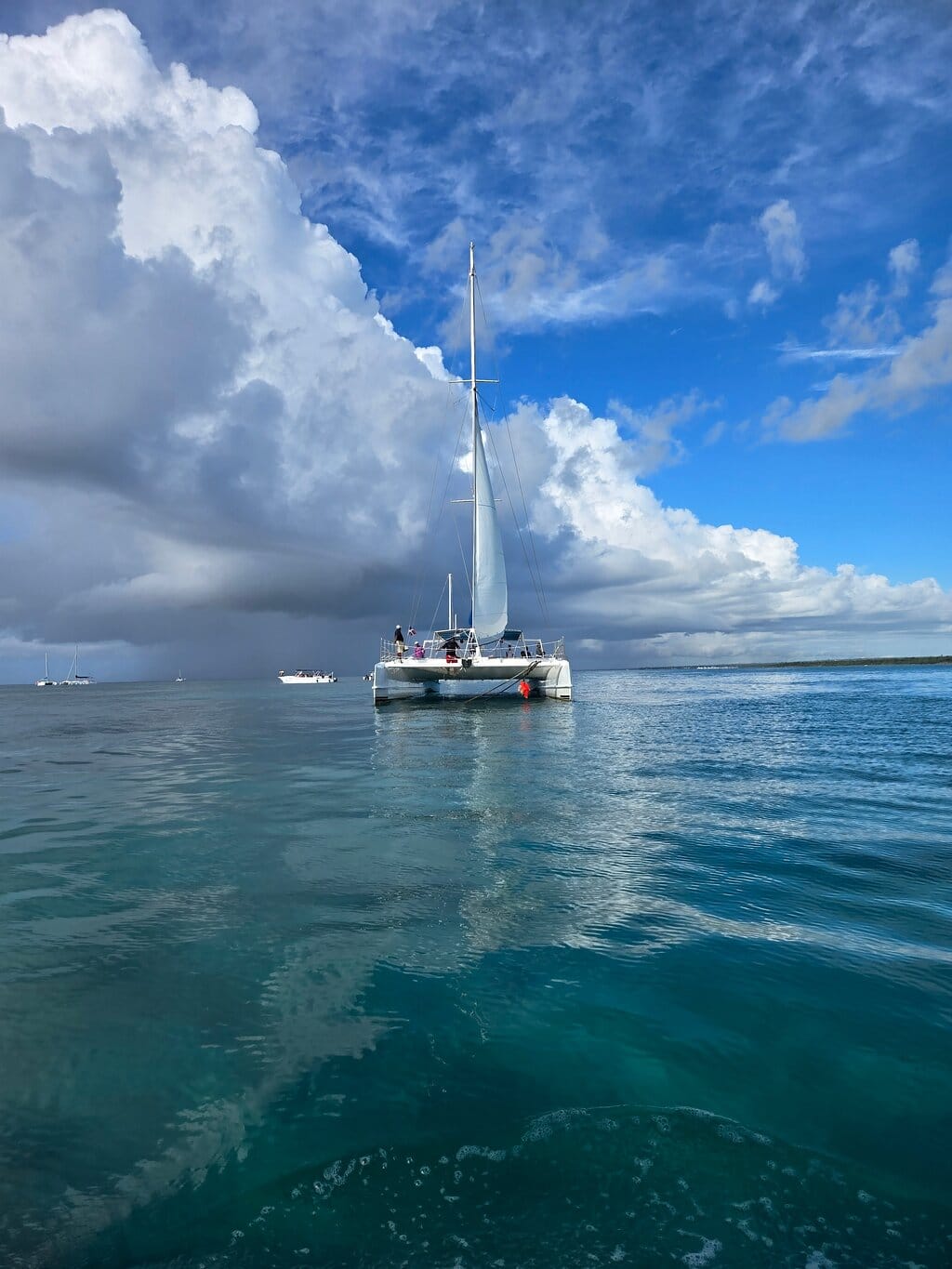 White catamaran anchored in calm waters under big clouds, with other boats in the distance