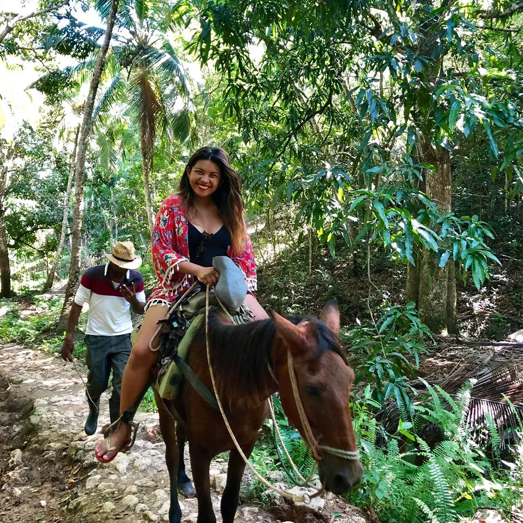 Smiling tourist riding a horse along a stone trail in the jungle, accompanied by a guide in a hat